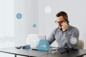 Professional man multitasks with laptop and smartphone in home office environment.