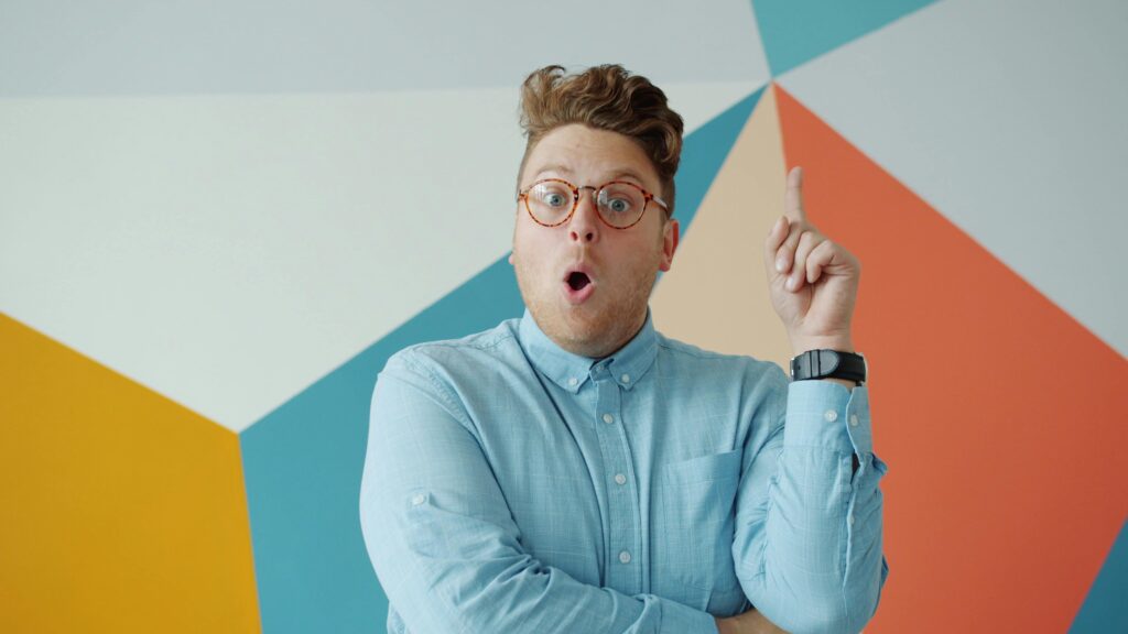 A surprised man in glasses points at a colorful geometric wall, conveying a sense of discovery.